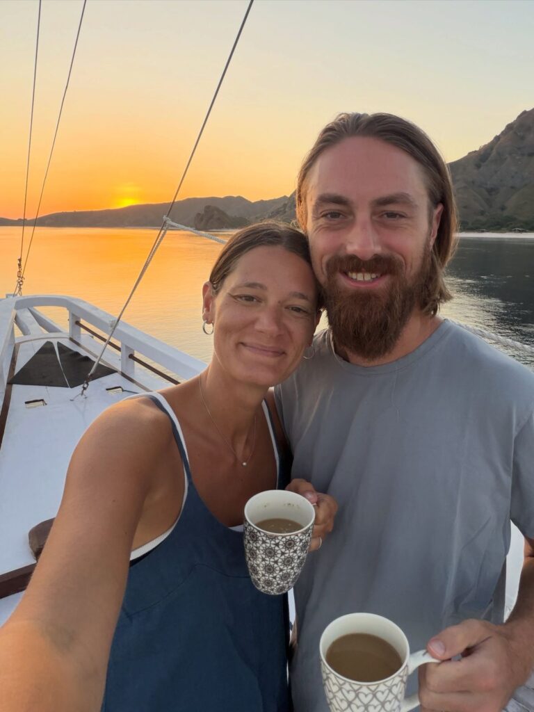 Couple drinking coffee on the deck of a Komodo liveaboard boat at sunrise