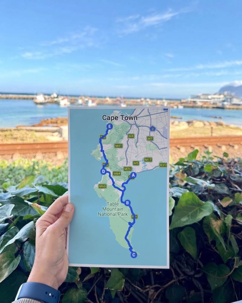 Cape Town itinerary route map from Camps Bay through Table Mountain National Park to Cape Point, held up in front of Kalk Bay harbour