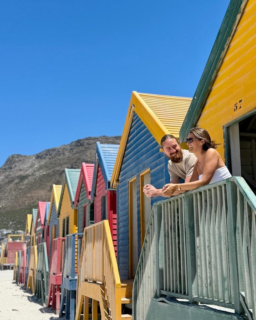 Couple laughing on the porch of a colorful Victorian beach hut at Muizenberg beach