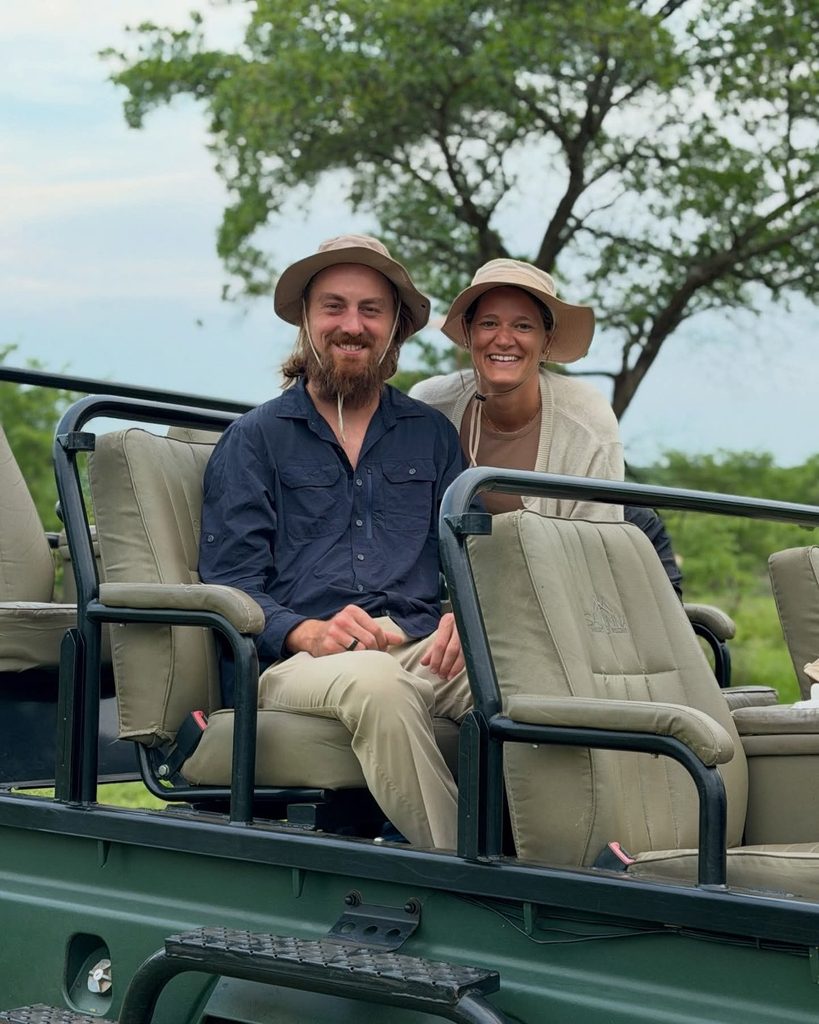 Couple in safari hats smiling from an open-sided game vehicle, comparing Sabi Sands vs Kruger National Park safari experiences